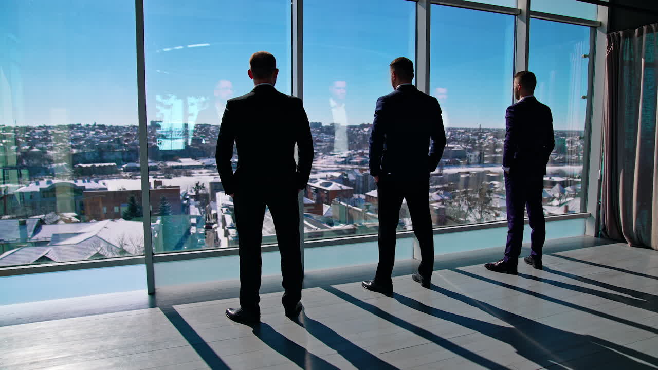 Elegant businessmen looking through office window. Back view of colleagues group rest at break. Business people in suits have a conversation near window.