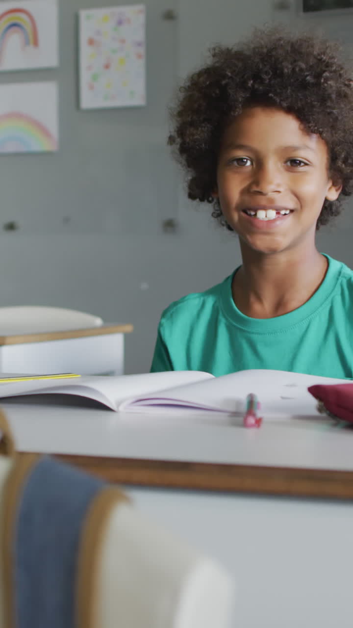 video de un niño biracial feliz sentado en un escritorio en el aula