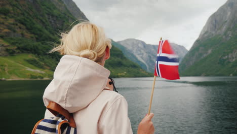 Eine-Person-Mit-Einer-Norwegischen-Flagge-In-Der-Hand-Reist-Auf-Einem-Schiff-Auf-Einem-Malerischen-Fjord
