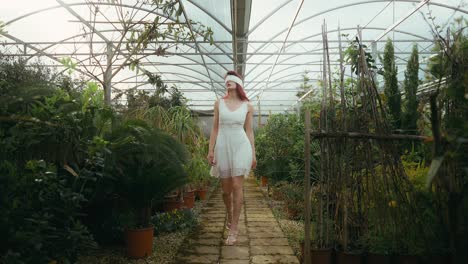 cinematic-low-angle-trucking-shot-of-young-woman-in-white-dress-and-blindfolded-walking-in-a-greenhouse-of-plants