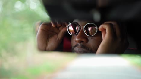reflejo del espejo trasero del camión del hombre africano poniéndose gafas de sol sentado dentro, primer plano de la cara
