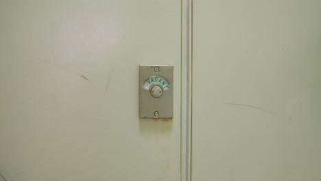 Slow-motion-wide-shot-of-bathroom-stall-door-changing-from-"Vacant"-to-"Engaged