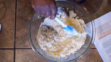 mixing flour and egg batter with spatula in home kitchen, overhead close up