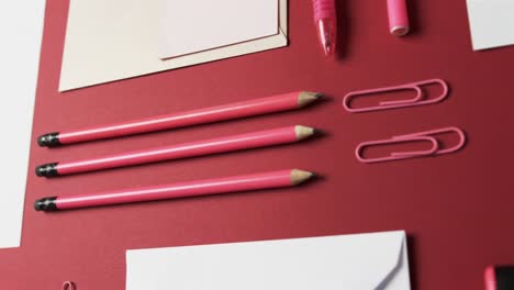 Close-up-of-pens,-pencils-and-stationery-arranged-on-red-background,-in-slow-motion