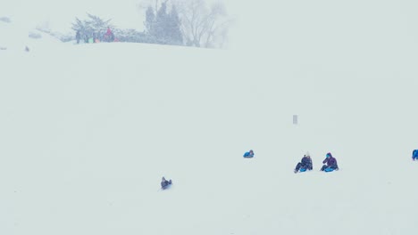 kids sliding down a steep snow covered hill during a winter storm