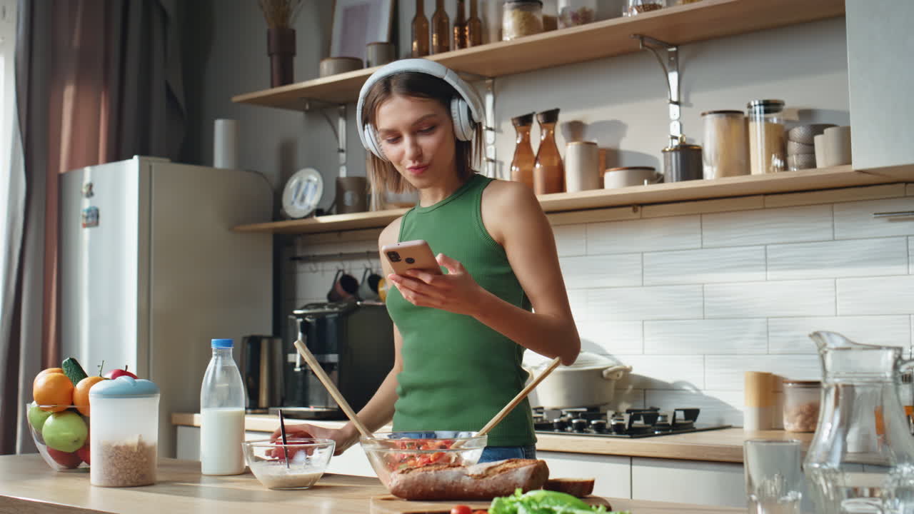 Woman in kitchen listening to music and using smartphone
