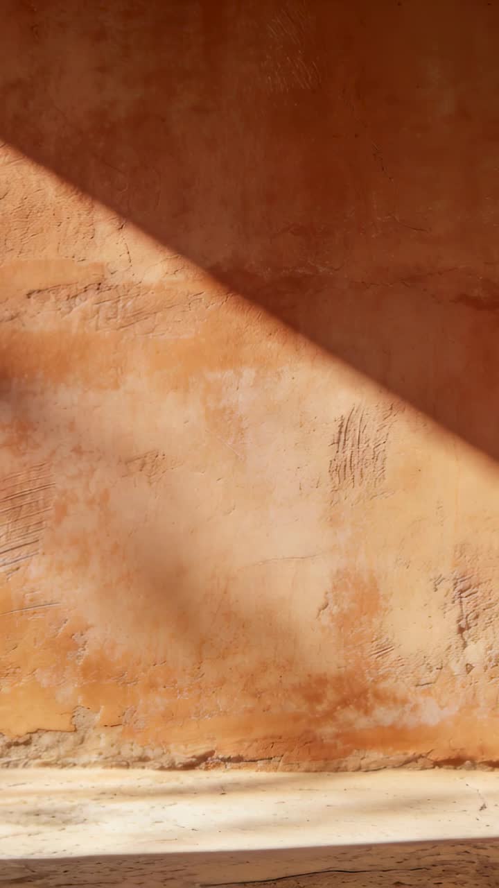 Video verticale: Luce solare che si sposta mentre il sole si muove su una parete di argilla in una stanza, mostrando segni di usura e una sporgenza.