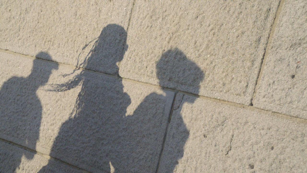 Shadow of three pedestrians walking at sunset. Shot against a brick wall on a summer day in slow motion.