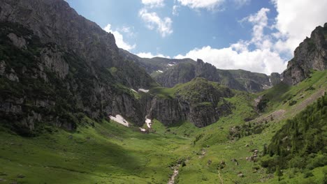 lush green valley in bucegi mountains with rocky cliffs and waterfall