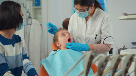 pediatric dentist with mask treating teeth to little girl patient