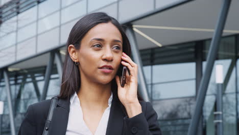 mujer de negocios que viaja al trabajo hablando por teléfono móvil fuera de un moderno edificio de oficinas