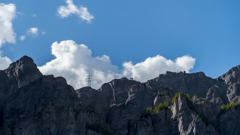 Mountain peak in Leukerbad named Gemmi. The cable car ascends the mountain. Power poles are visible. Time-lapse of clouds in the sky. The natural landscape is in bloom. Tourist area