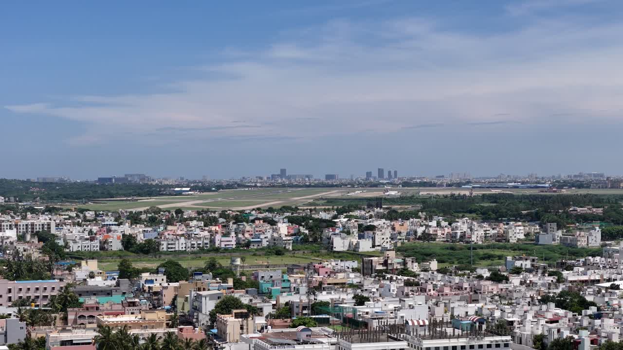 A wide, daytime shot overlooking a dense residential area with an airport runway in the mid-ground and a modern city skyline on the horizon