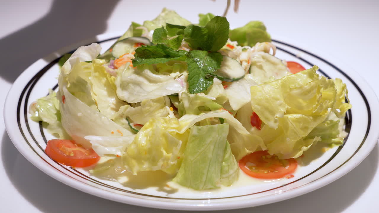 Close-up of a platter of vegetable salad, a mixture of cucumbers, lettuce, tomatoes, carrots, topped with mint, and drizzled with vinaigrette