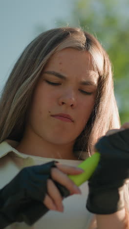joven adulto con cabello rubio luchando para ajustar la boquilla de la bomba de aire verde mientras está de pie al aire libre en un día soleado, el fondo cuenta con árboles verdes exuberantes