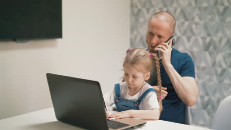 father-answers-call-while-girl-does-homework-on-laptop