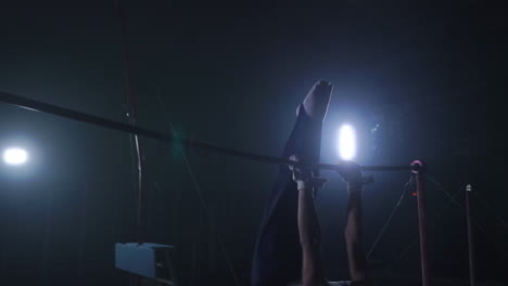 gymnast on a dark background on the crossbar performs spins and jumps over himself in the air in slow motion and around the smoke