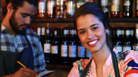 portrait of smiling barmaid with barman in background