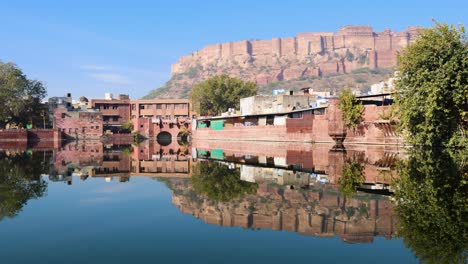 Lago-Prístino-Y-Tranquilo-Con-Reflejo-Del-Histórico-Fuerte-De-Mehrangarh-Y-Casas-Alrededor-Por-La-Mañana.-El-Vídeo-Se-Toma-En-Gulab-Sagar-Talab-Jodhpur-Rajasthan-India.