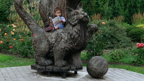 child reading a book on a wooden cat sculpture in a park
