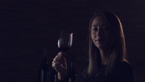 mujer morena sosteniendo una copa de vino tinto, mirando directamente a la cámara en un estudio oscuro