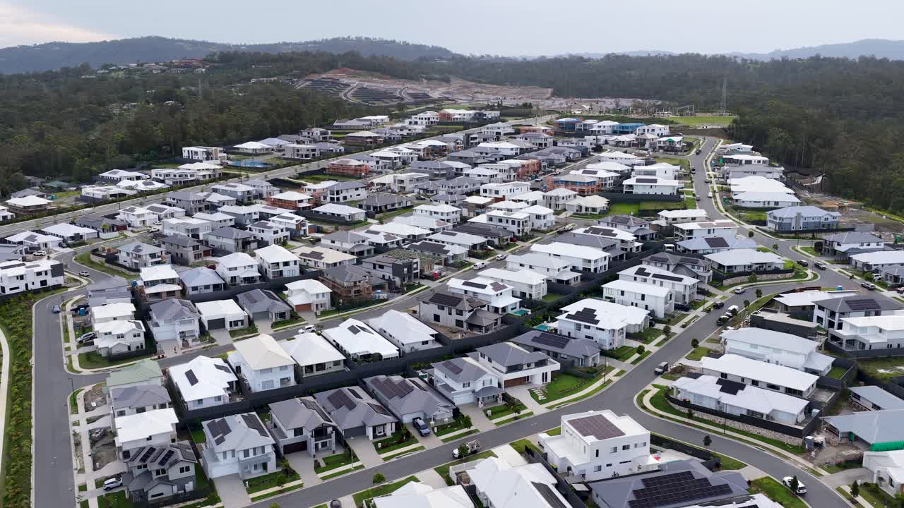 Drone slowly glides over contemporary suburban homes, lush forest backdrop, soft daylight, wide perspective