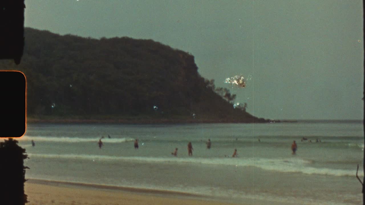 Filmato vintage Super 8 di persone che nuotano godendosi le onde dell'oceano in estate sulla costa della penisola di Durras Beach, South Coast, Australia: effetti di luce, viaggio retrò, turismo