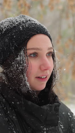 primer plano de una mujer joven con gorra negra y abrigo de invierno cubierto de copos de nieve frescos que se siente enfocada en la guitarra, con árboles nevados serenos borrosos en el fondo