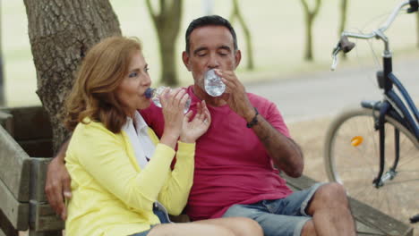 senior couple drinking water in park after cycling