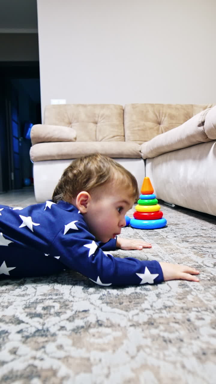 Lovely child lies on the floor looking under the sofa. Kid rises and sits on his knees. Black cat sitting behind watching a baby. Vertical video