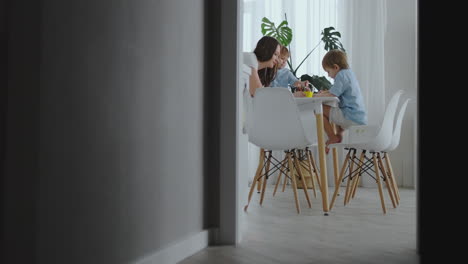 mom helps sons learn to draw doing homework preschool preparation at home sitting in the white kitchen. two brothers draw a portrait of mom together