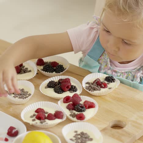 Mädchen-Legt-Beeren-Auf-Muffins-Auf-Den-Tisch