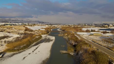 flying over a winter landscape and towards a pedestrian bridge over a river through a park - aerial view