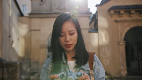 Portrait-Shot-Of-The-Pretty-Young-Female-Photograph-Taking-A-Photo-With-Professional-Camera-And-Then-Smiling-To-The-Camera-Among-Historical-Buildings