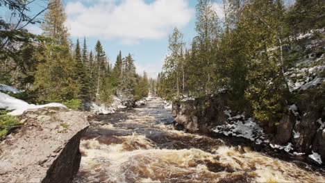 Vibrant-winter-scene-looking-down-on-a-sun-drenched-river-winding-between-snow-covered-banks-lined-with-towering-pines