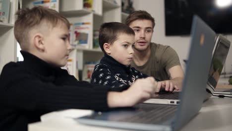 joven profesor atractivo que muestra a dos niños pequeños cómo usar aparatos como computadoras portátiles. tecnologías y progreso.