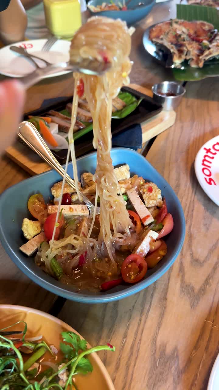 Tangan mengangkat mi Yum Woon Sen dari salad Thailand yang semarak di restoran terang di Bangkok.