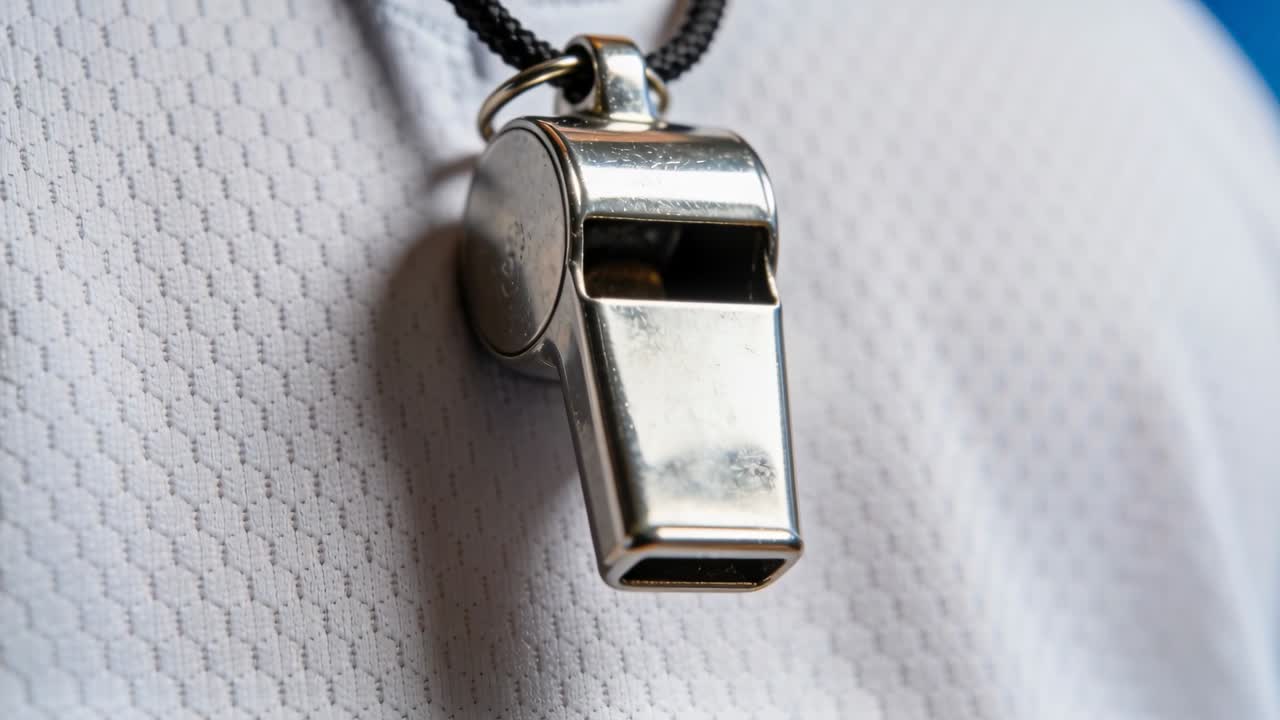 Fischietto d'argento oscillante su un cordino su una maglia bianca a bordo campo, il movimento di chi lo indossa provoca un luccichio.