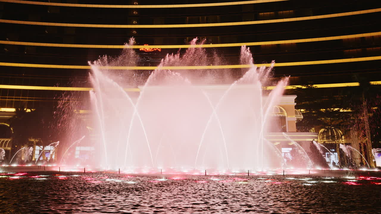 Espectacular show de fuentes danzantes iluminadas por la noche frente a un edificio moderno.