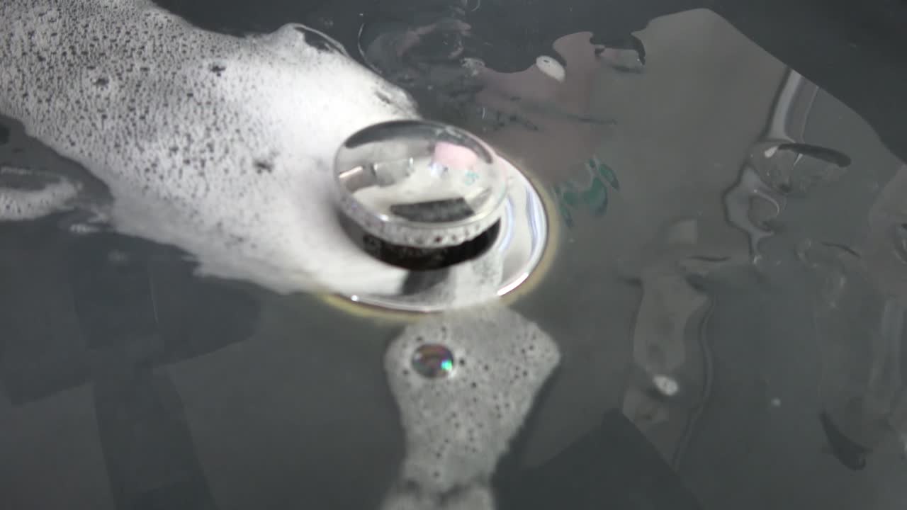 팝업 금속 배수구가 있는 검은색 싱크대의 흰색 거품 거품