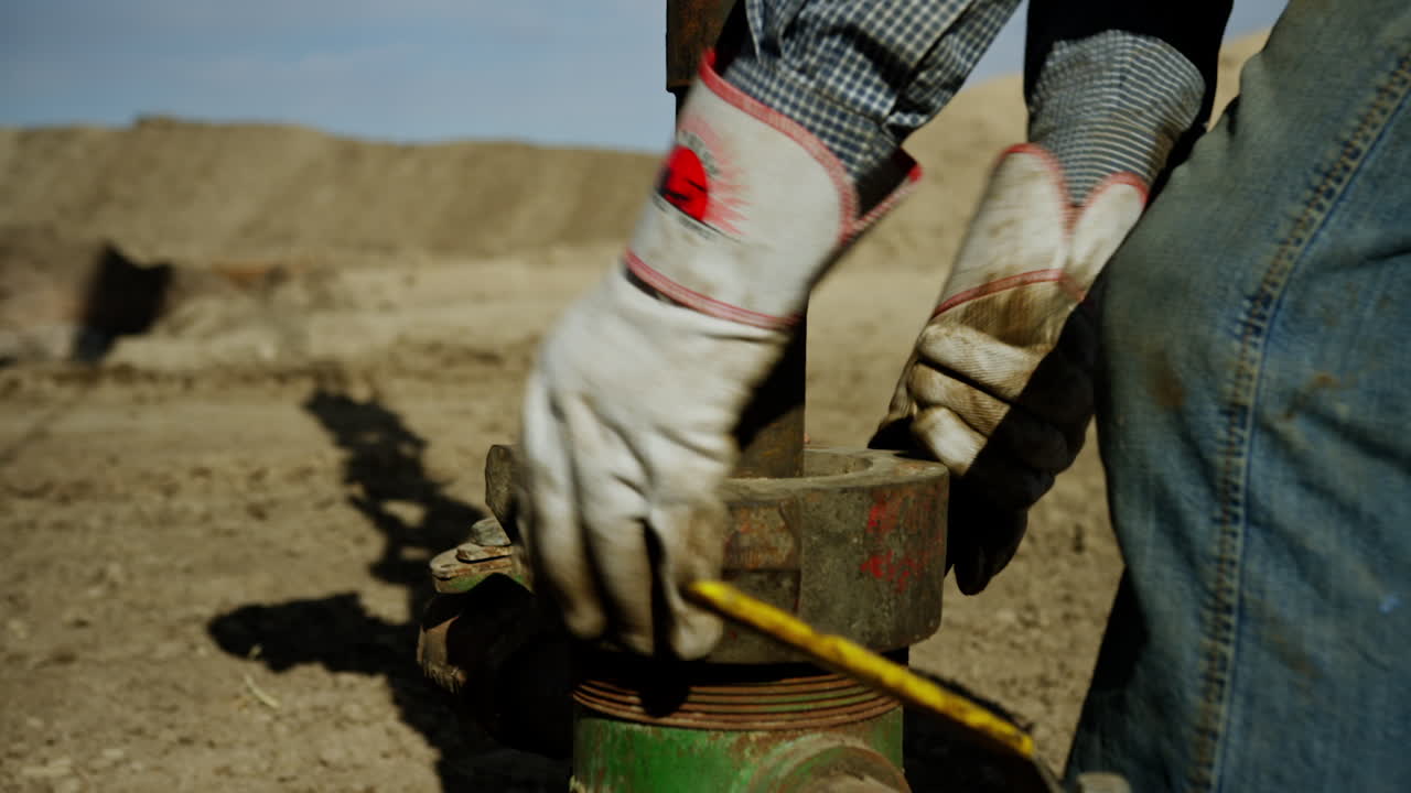 Unrecognized worker wearing dirty jeans rotates the metal element on the pipe. Arranging equipment for oil or gas production.