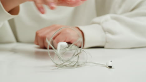 tangled wires on table close-up. trying to untangle many messy cables.young woman trying to untangle the white headphones.