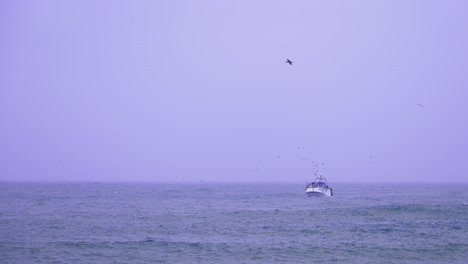 Small-fishing-boat-on-the-Atlantic-Ocean-during-a-rainy-cold-and-windy-day,-slow-motion-shot-with-seagulls-flying-near-the-vessel