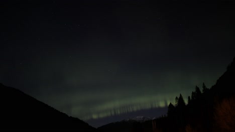 Luces-Del-Norte-De-Intensidad-Media-Jugando-Lentamente-Sobre-La-Silueta-De-La-Montaña-Y-Las-Copas-De-Los-árboles-En-Stamnes-En-El-Oeste-De-Noruega