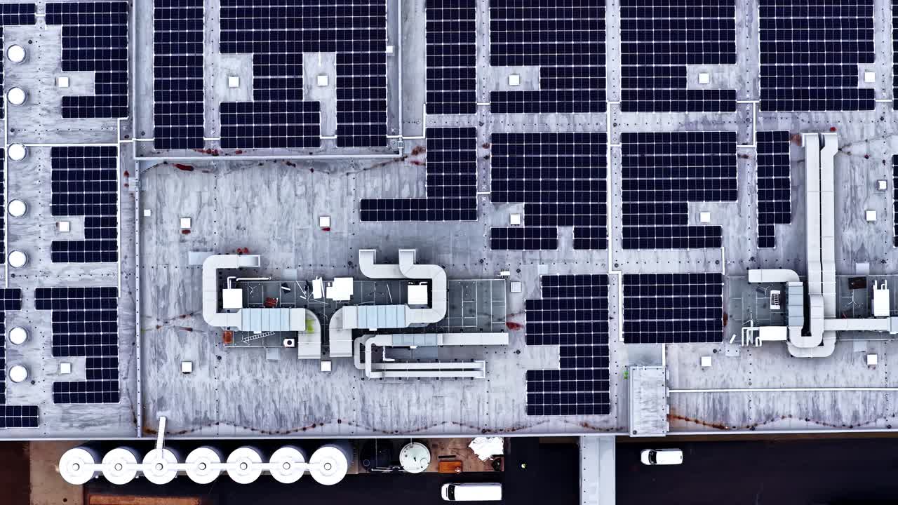 Droneoptagelse af solcellepaneler på erhvervstag med ventilationssystemer.