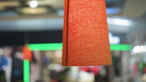 primer plano de una lámpara colgante naranja iluminada con una sombra texturizada, colgada en el interior contra un fondo borroso de verde y otras luces