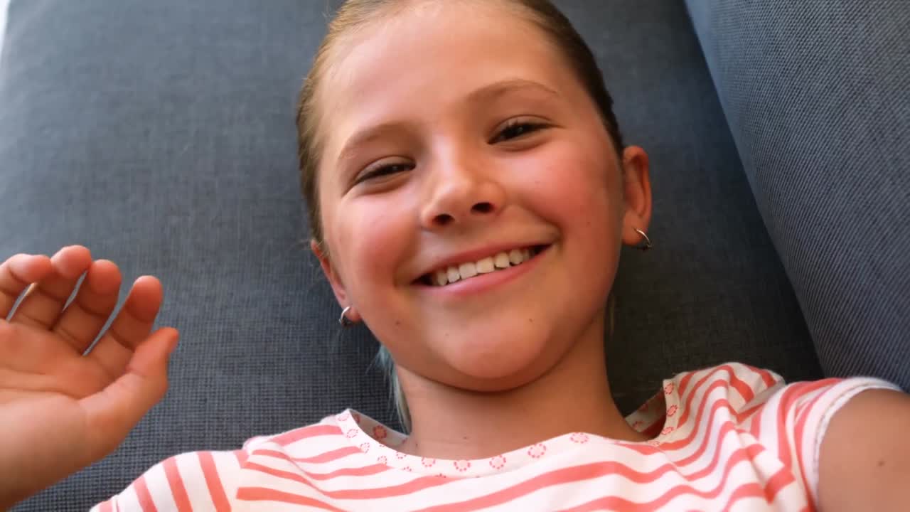 Portrait of cute girl waving hand on sofa