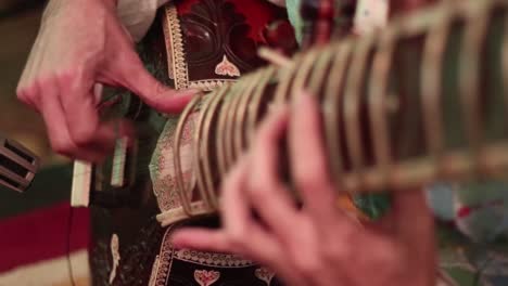 close up of mans hands playing an indian instrument called a sitar