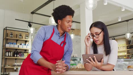 Video-of-happy-diverse-female-owner-and-male-waiter-working-with-tablet-at-cafe-shop