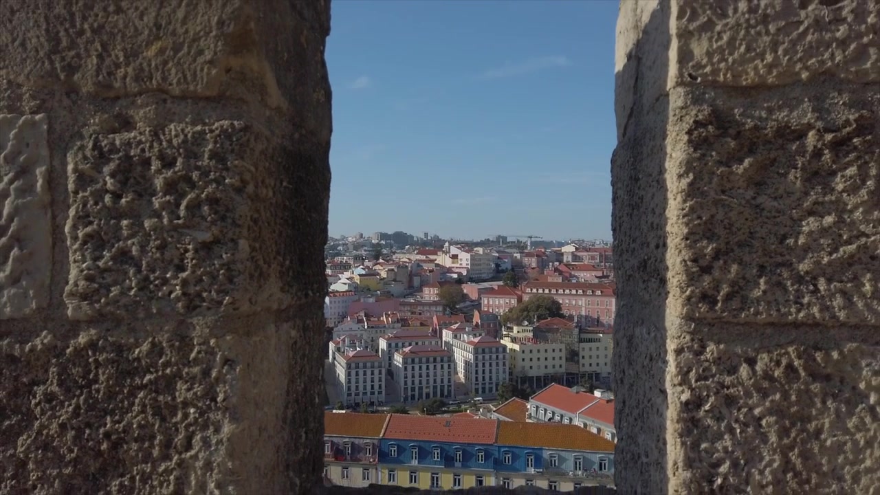Ripresa in allontanamento attraverso un muro del castello storico di Lisbona, che incornicia la vivace città sottostante, ideale per un'introduzione di viaggio.